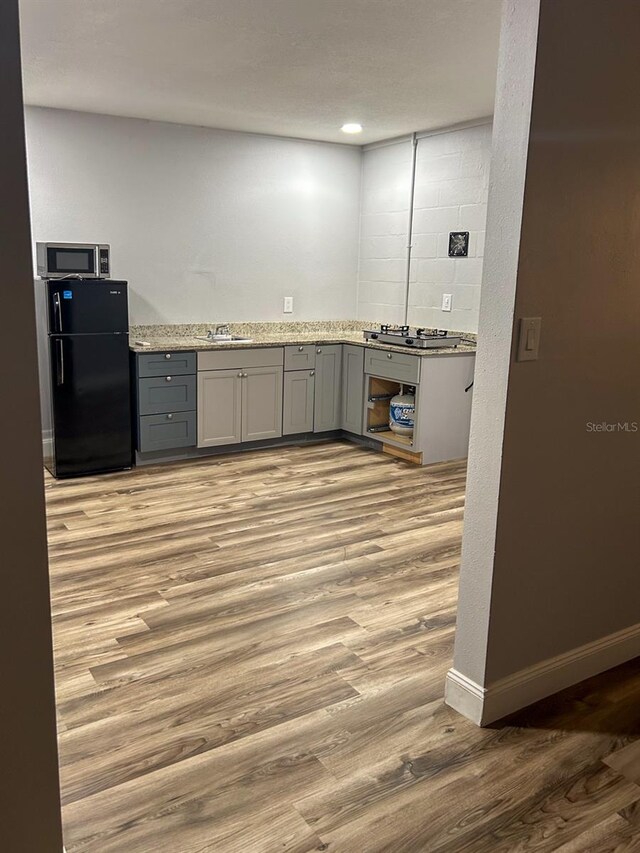 kitchen featuring black fridge, sink, gray cabinetry, light hardwood / wood-style flooring, and light stone countertops