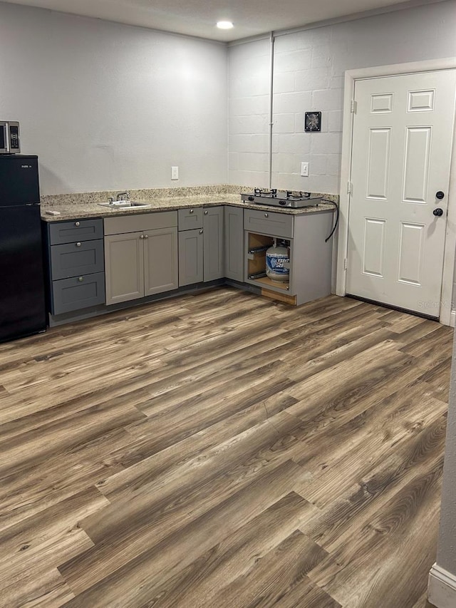 kitchen with gray cabinetry, dark wood-type flooring, light stone counters, stainless steel gas stovetop, and black fridge