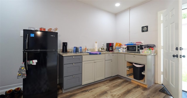 kitchen with light wood-type flooring, gray cabinetry, light stone countertops, and black refrigerator