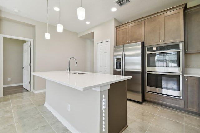 kitchen featuring a kitchen island with sink, sink, light tile patterned floors, appliances with stainless steel finishes, and decorative light fixtures