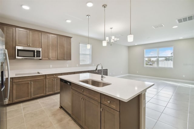 kitchen with a center island with sink, hanging light fixtures, sink, light tile patterned floors, and appliances with stainless steel finishes