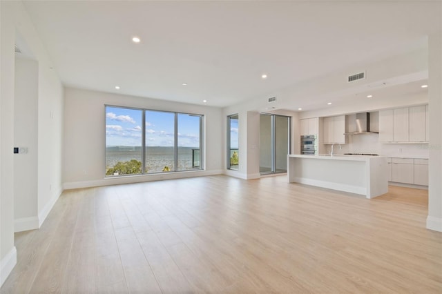 unfurnished living room featuring light hardwood / wood-style flooring, a water view, and sink