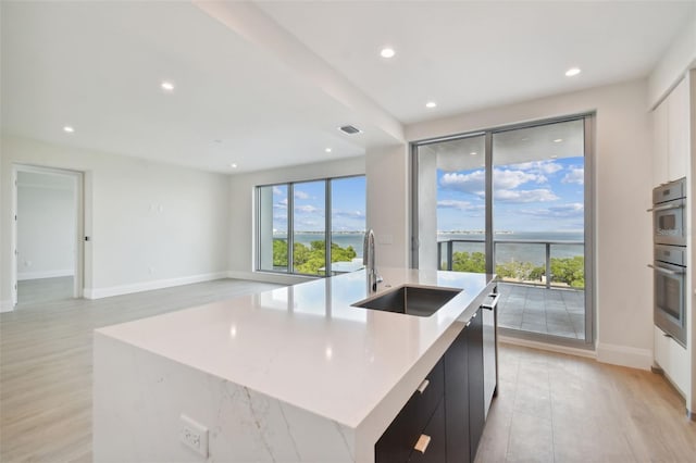 kitchen with appliances with stainless steel finishes, light wood-type flooring, sink, and a large island with sink