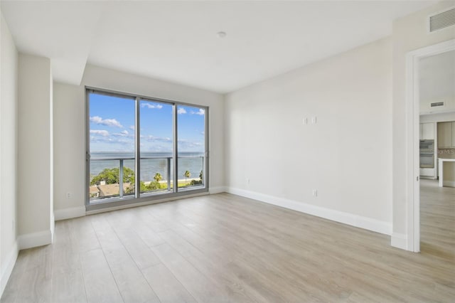 unfurnished room featuring a water view and light hardwood / wood-style floors