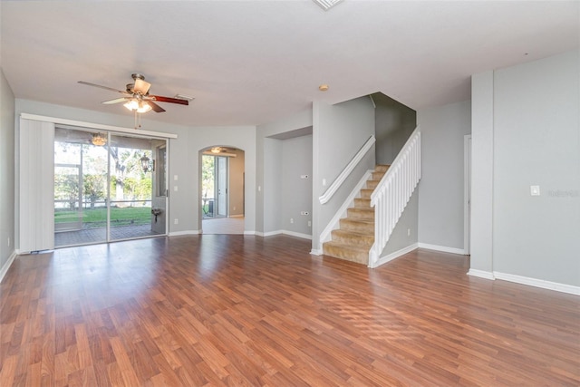 empty room with baseboards, arched walkways, a ceiling fan, stairway, and wood finished floors