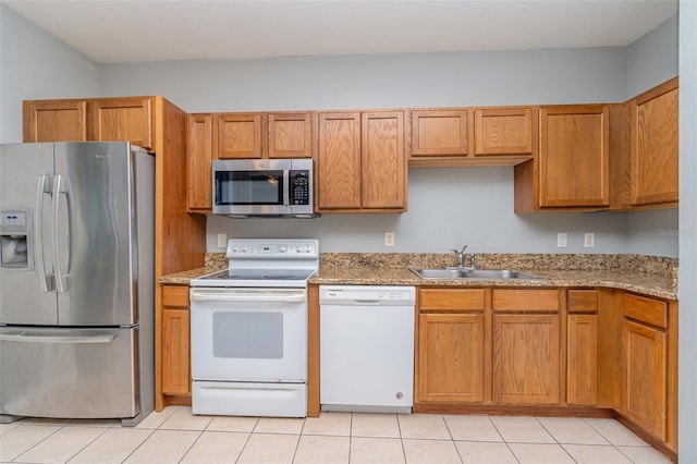 kitchen with appliances with stainless steel finishes, brown cabinets, a sink, and light tile patterned flooring