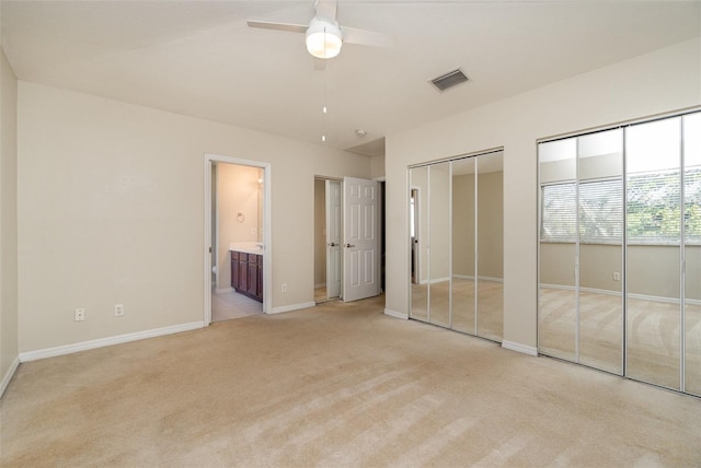 unfurnished bedroom with connected bathroom, light carpet, visible vents, baseboards, and multiple closets