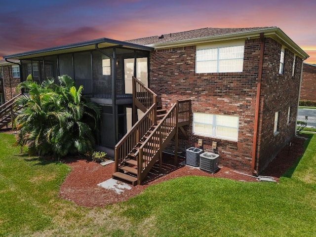 back house at dusk with a sunroom, cooling unit, and a lawn