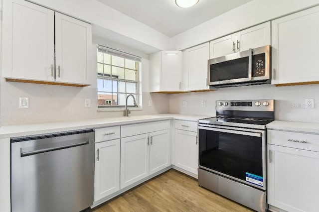 kitchen with sink, stainless steel appliances, white cabinetry, and light hardwood / wood-style floors