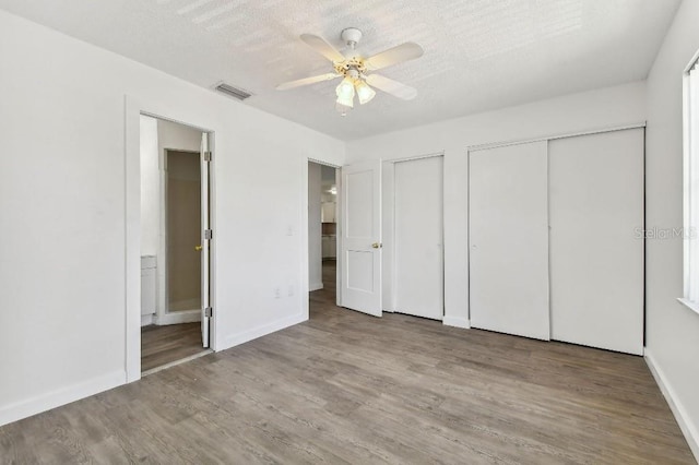 unfurnished bedroom with ceiling fan, a textured ceiling, multiple closets, and hardwood / wood-style flooring