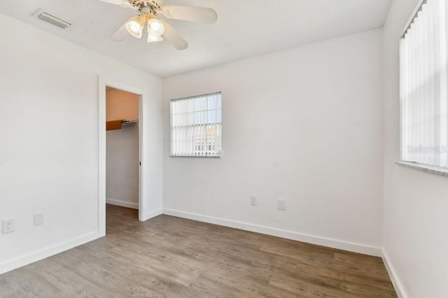 unfurnished bedroom featuring ceiling fan, wood-type flooring, a walk in closet, and a closet