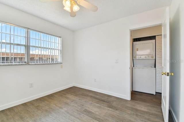 empty room with ceiling fan, stacked washer and clothes dryer, and dark wood-type flooring