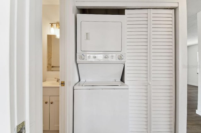 clothes washing area featuring hardwood / wood-style floors, sink, and stacked washer and clothes dryer