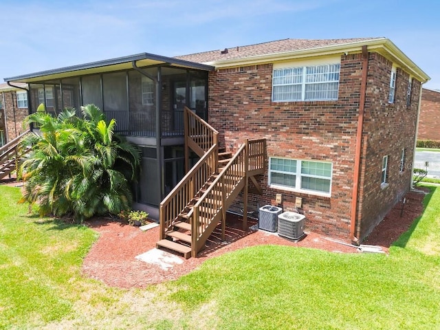 rear view of house with a lawn, central air condition unit, and a sunroom