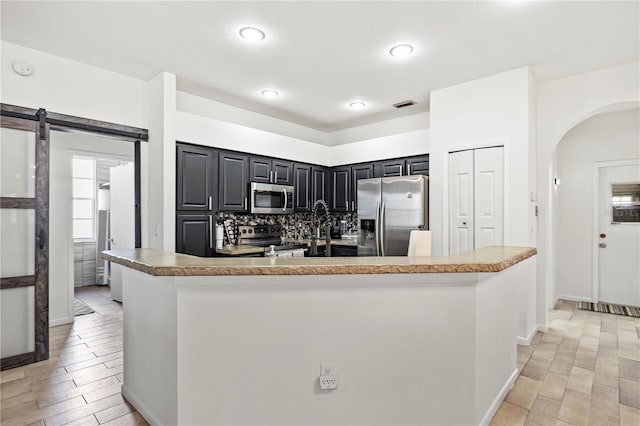 kitchen featuring tasteful backsplash, a barn door, light tile patterned flooring, a center island, and stainless steel appliances