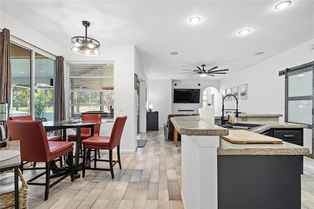 kitchen with ceiling fan with notable chandelier, pendant lighting, light hardwood / wood-style flooring, sink, and a barn door