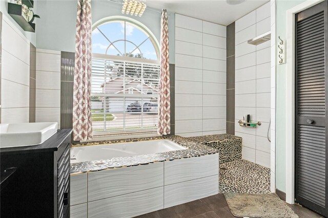 bathroom featuring tile walls, a relaxing tiled tub, and vanity