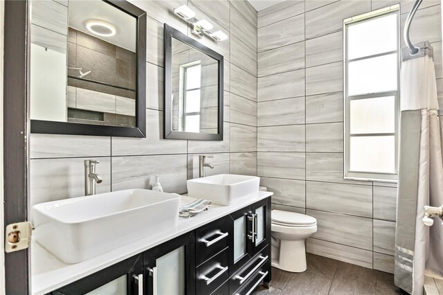 bathroom featuring dual bowl vanity, tile walls, and toilet