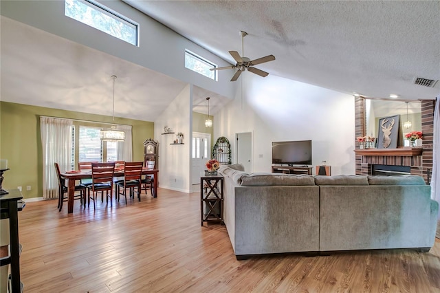 living room with a textured ceiling, a brick fireplace, ceiling fan, and light hardwood / wood-style flooring