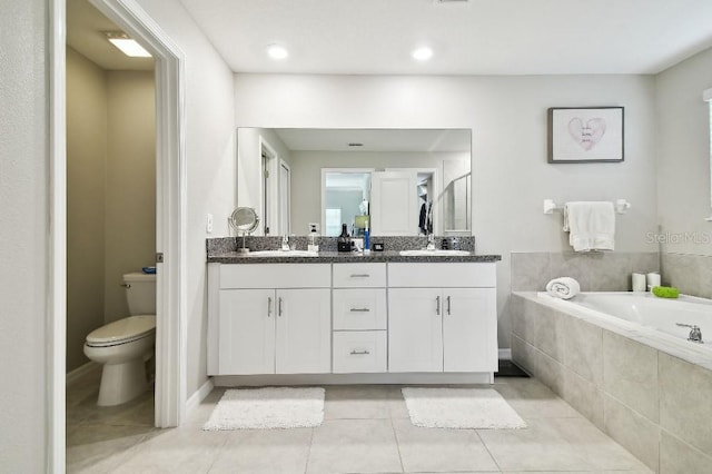 bathroom with tile patterned flooring, vanity, tiled tub, and toilet