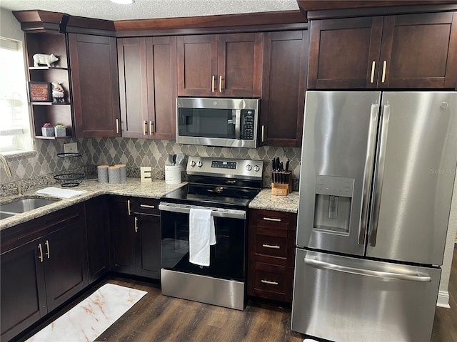 kitchen with sink, dark wood-type flooring, tasteful backsplash, light stone counters, and appliances with stainless steel finishes