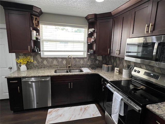 kitchen with appliances with stainless steel finishes, light stone counters, dark brown cabinets, sink, and dark hardwood / wood-style floors