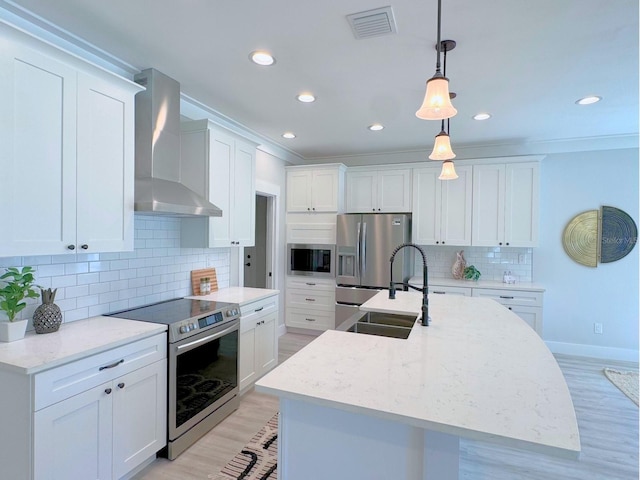 kitchen featuring appliances with stainless steel finishes, wall chimney exhaust hood, white cabinetry, and decorative light fixtures