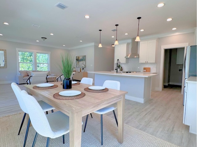 dining area featuring light wood-type flooring, crown molding, and sink