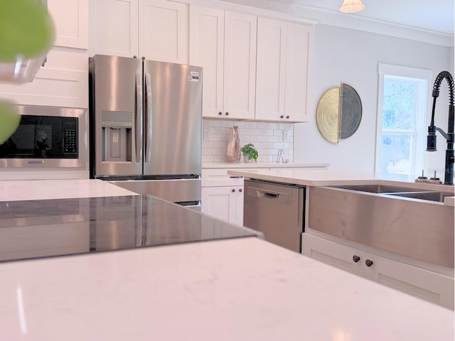 kitchen with backsplash, white cabinetry, appliances with stainless steel finishes, and ornamental molding