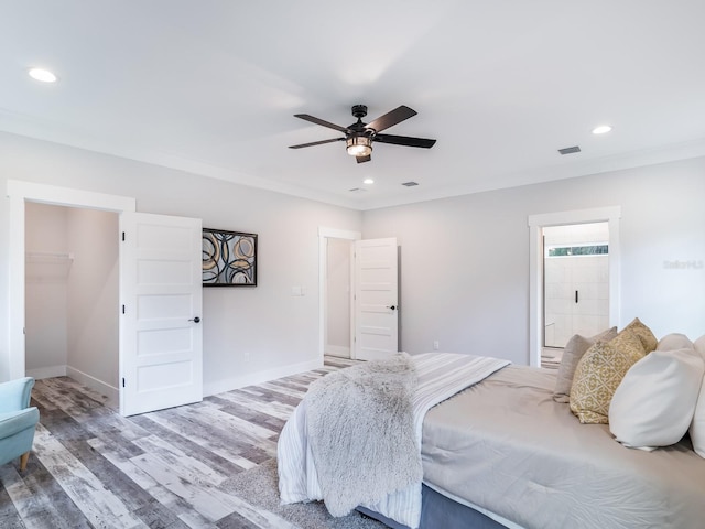 bedroom featuring hardwood / wood-style flooring, ceiling fan, a closet, ornamental molding, and a walk in closet