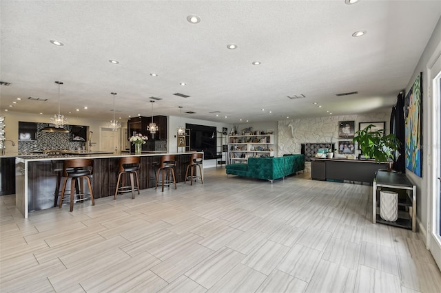 interior space featuring a stone fireplace, a kitchen bar, hanging light fixtures, a large island, and a textured ceiling