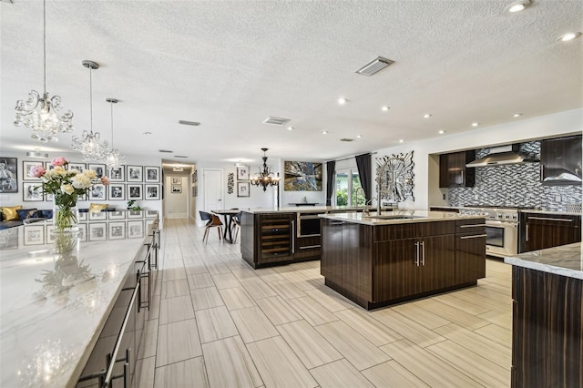 kitchen with wall chimney range hood, dark brown cabinets, pendant lighting, and a spacious island