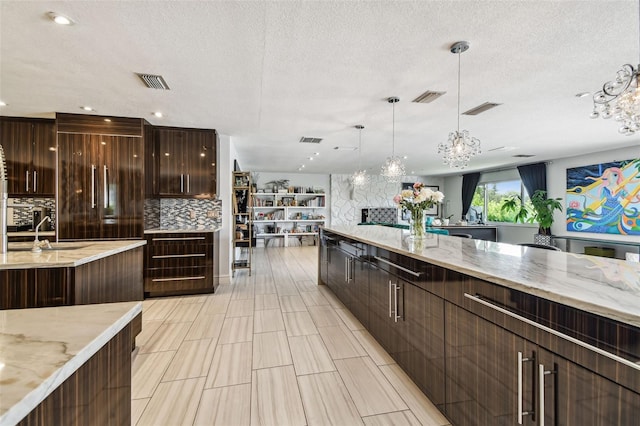 kitchen with decorative light fixtures, light stone countertops, sink, and decorative backsplash