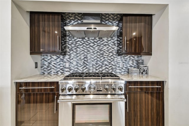 kitchen featuring dark brown cabinetry, stainless steel gas range, decorative backsplash, and wall chimney range hood