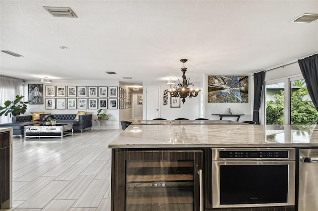 kitchen featuring pendant lighting, light stone counters, a kitchen island, beverage cooler, and a chandelier