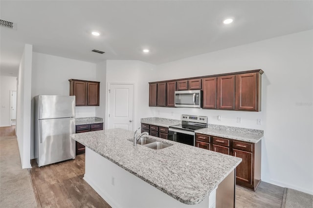 kitchen with an island with sink, sink, carpet floors, light stone countertops, and appliances with stainless steel finishes