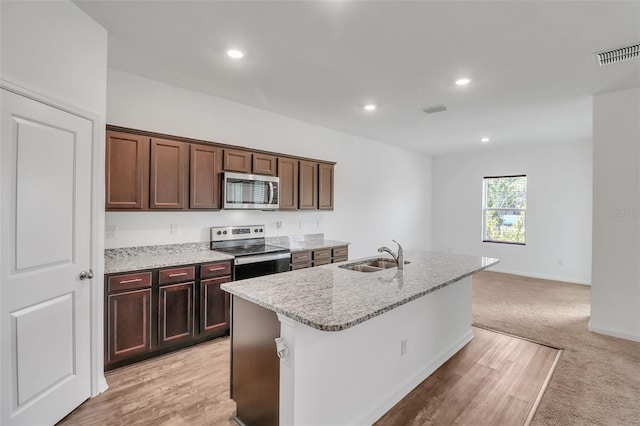 kitchen with sink, light carpet, appliances with stainless steel finishes, light stone countertops, and a kitchen island with sink