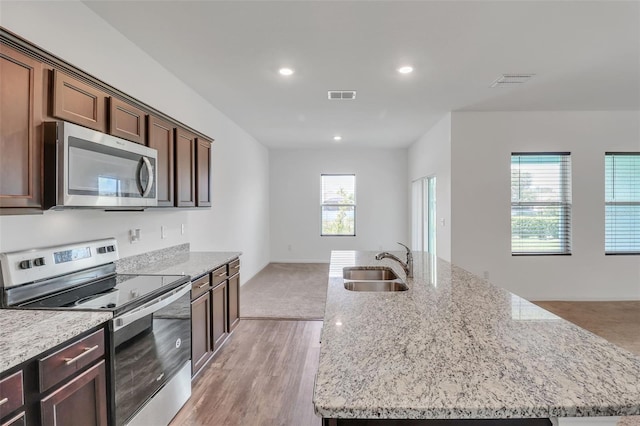 kitchen with light stone counters, an island with sink, stainless steel appliances, and sink