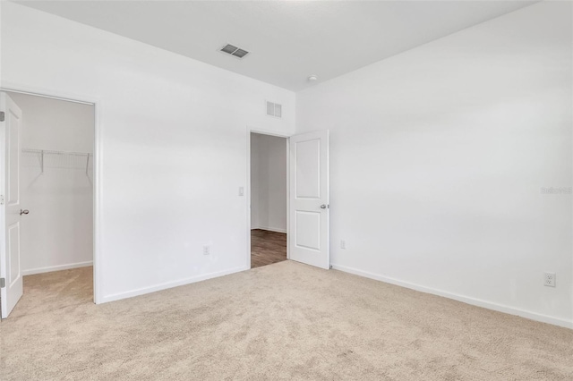 unfurnished bedroom with a walk in closet, light colored carpet, and a closet