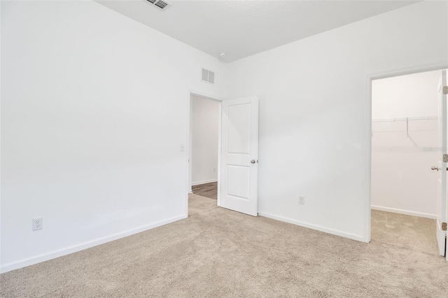 unfurnished bedroom with a spacious closet, light carpet, and a closet