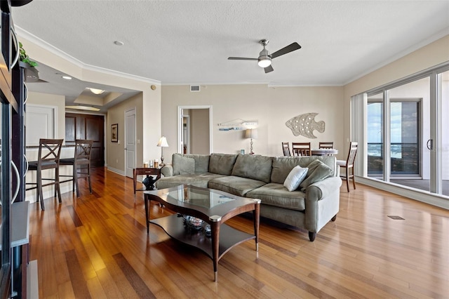 living room with ceiling fan, light hardwood / wood-style floors, ornamental molding, and a textured ceiling