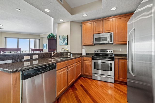 kitchen featuring a textured ceiling, stainless steel appliances, sink, hardwood / wood-style flooring, and dark stone countertops