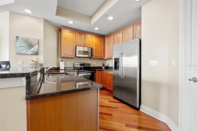 kitchen featuring kitchen peninsula, appliances with stainless steel finishes, light wood-type flooring, sink, and dark stone countertops