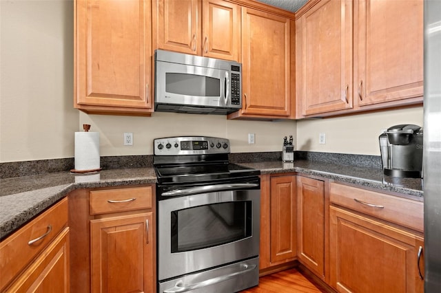 kitchen with dark stone countertops, stainless steel appliances, and light hardwood / wood-style flooring