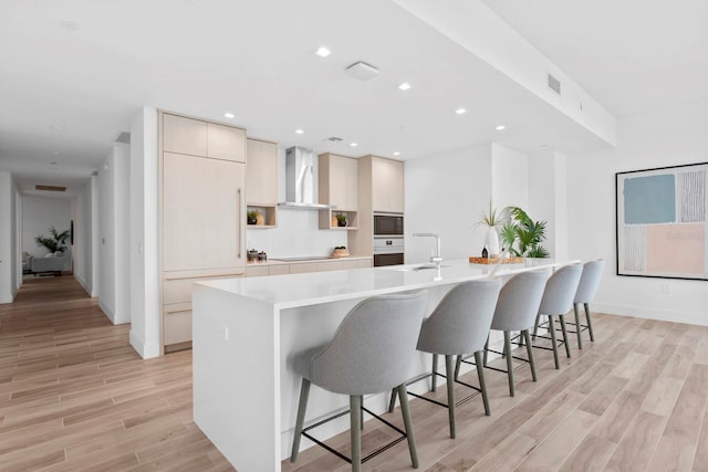 kitchen featuring black appliances, a kitchen bar, wall chimney range hood, a large island, and light hardwood / wood-style flooring