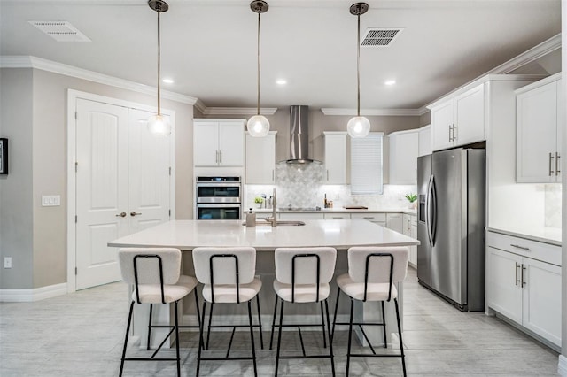 kitchen with white cabinetry, appliances with stainless steel finishes, a center island with sink, and wall chimney range hood