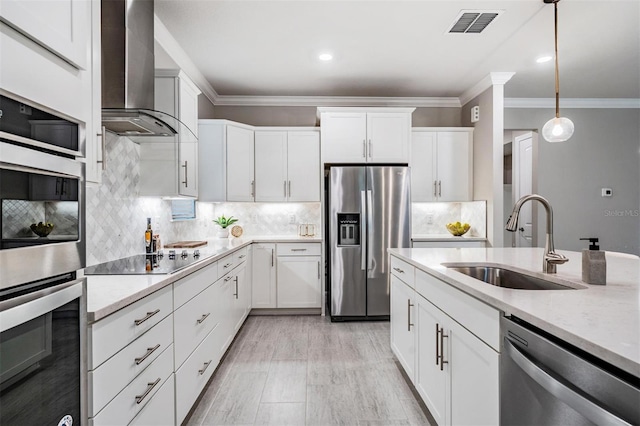 kitchen featuring appliances with stainless steel finishes, wall chimney exhaust hood, decorative light fixtures, white cabinetry, and sink