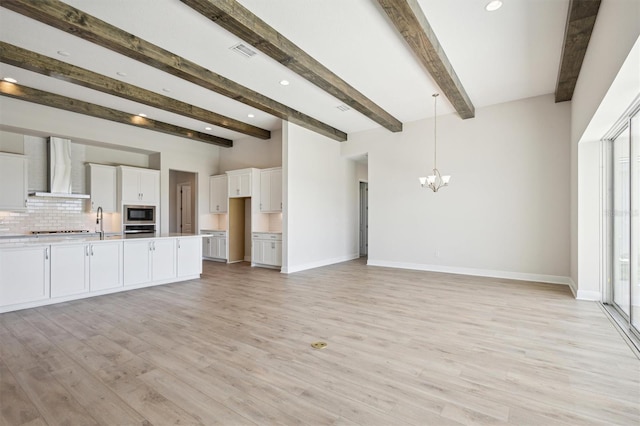 kitchen featuring wall chimney range hood, beam ceiling, light hardwood / wood-style flooring, hanging light fixtures, and white cabinetry