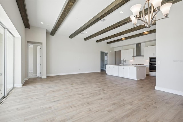 unfurnished living room with an inviting chandelier, light hardwood / wood-style flooring, beam ceiling, and sink