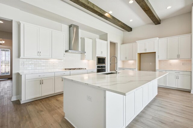 kitchen featuring light wood-type flooring, white cabinetry, a sink, stainless steel appliances, and wall chimney exhaust hood